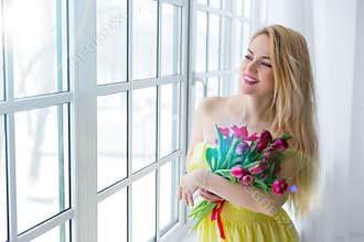 Young happy woman smiling with tulip bunch in yellow dress. 8 march international womens day.