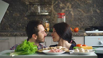 Beautiful smiling couple play and kiss above the table with vegetables while cooking in kitchen