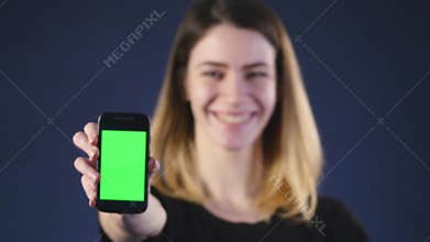 Focus on mobile phone. Young woman hands showing blank smartphone screen isolated on green background and pointing on