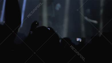 Audience with hands raised at a music festival and lights streaming down from above the stage. Blured background.
