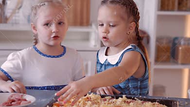 Little girls sprinkle pizza with cheese