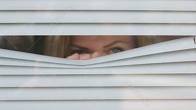 Woman looking out the window through the blinds to the street, spying. suspected