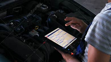 Mechanic in a auto repair shop checking engine using a digital tablet