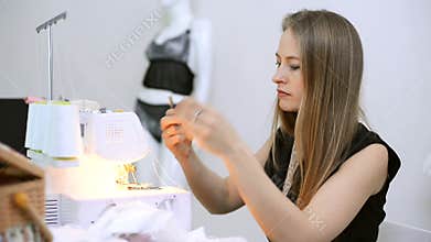 Seamstress sits and white thread inserts into the overlock.