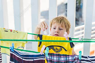 A little boy helps her mother to hang up clothes