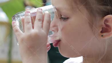 Close-up of a little cute girl drinking pure water from a glass