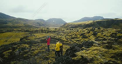 Aerial view of group of tourists hiking on lava fields in Iceland. Woman photographer holding camera, waiting friends