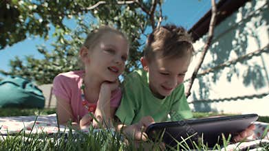 Cheerful kids watching tablet in garden