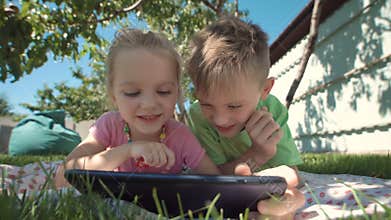 Cheerful kids watching tablet in garden