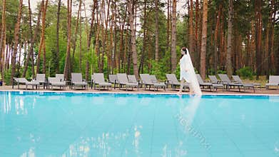 The bride with a long veil is walking around the pool. Wedding in a luxury hotel