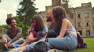 Students in campus sitting on grass, talking and laughing.