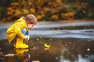 Happy child girl with paper boat in puddle in autumn on natu