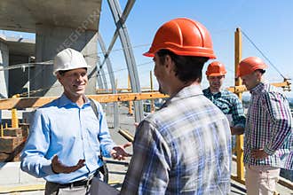 Builders Meeting On Construction Site Architect Talking With Contractor Over Group Of Apprentice