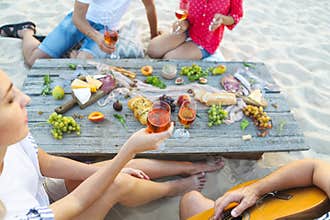 Young friends drinking rose wine on summer beach picnic