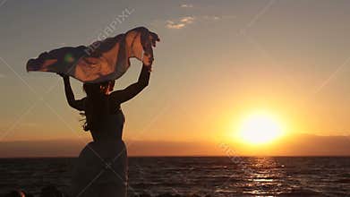 Silhouette of woman with scarf on beach at sunset