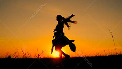Silhouette of young witch dancing at field