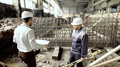 Professional engineers working together on construction site. Chief architect walking to worker standing near formwork