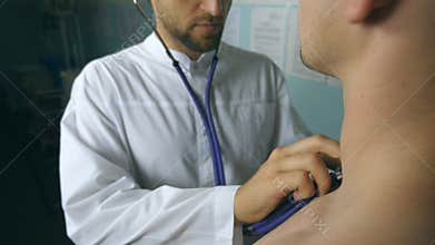 Portrait of handsome doctor examining patient with stethoscope. Young medical worker listening heartbeat of sick