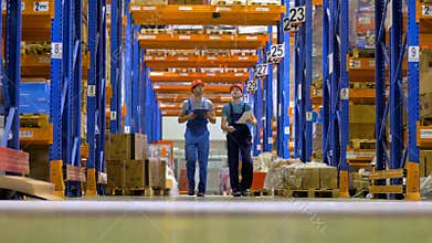 Two warehouse workers walk under high orange storage racks.