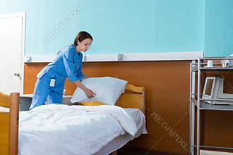 Female nurse holds a white pillow over the hospital bed in the h
