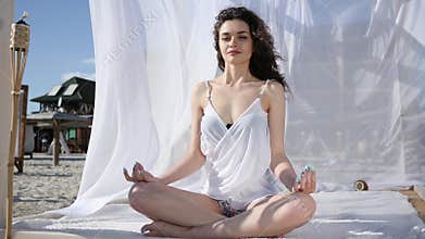 Girl in lotus position, in bungalow, relaxation on tropical islands, summer, wind develops hair and white cloth, sunny