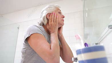 Senior Woman Checking Skin In Bathroom Mirror