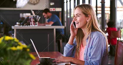 Woman In Cafe Working On Laptop And Answering Phone