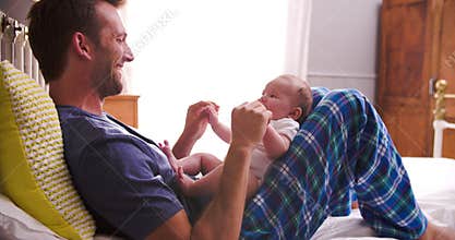 Father In Bed Playing With Newborn Baby Daughter
