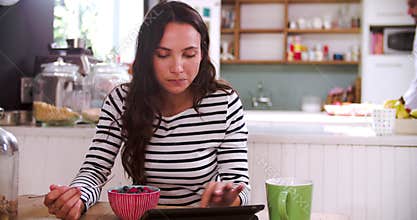 Young Woman Eating Breakfast Whilst Using Digital Tablet