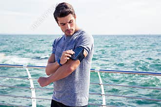 Male runner listening to music adjusting settings on armband for smartphone