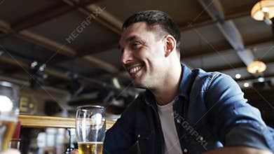 Happy young man drinking beer at bar or pub