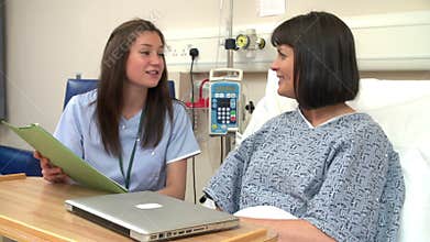 Nurse Sitting By Female Patient's Bed In Hospital