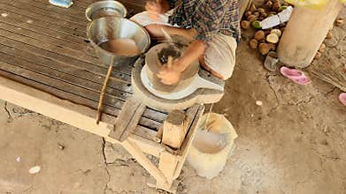 Upper view on woman sat cross-legged using hand-turned millstone to grind wet rice for making soaked rice flour 