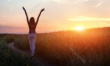 Free happy woman raising arms at sunset in the field