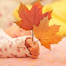 Newborn baby hand holding autumn leaves.
