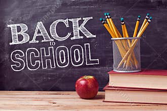 Back to school lettering with books, pencils and apple over chalkboard background