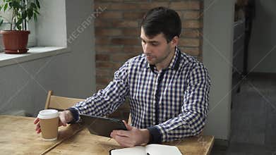 Man in the morning drinking coffee and working on the tablet.