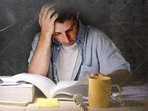 Young student at home desk reading studying at night with pile of books and coffee
