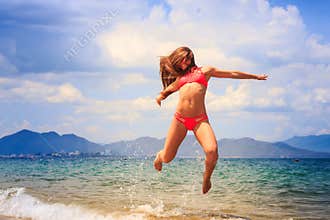 Blonde gymnast in bikini jumps over sea face closed with hair