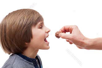 A small boy bites chocolate ball from man hand