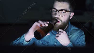 Man drinking beer and using PC