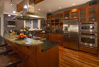 Contemporary upscale home kitchen interior with wood cabinets and floors, granite countertop and stainless steel appliances