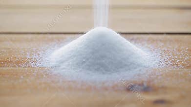 White sugar pouring into heap on wooden table