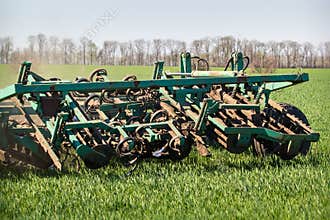 Closeup weeding-machine behind tractor on green wheat field