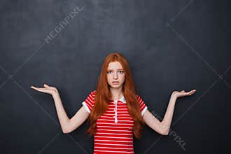 Confused woman holding copyspace on both palms over chalkboard background