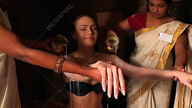 Woman having Ayurvedic spa treatment. Indian masseuse pouring oil of patient.