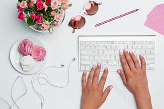 Office desk table with female hands, computer, supplies, flowers