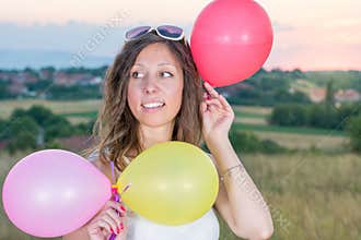 Young woman holding balloons at sunset