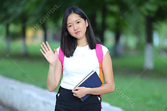 Young girl walking in the park looking at the camera and waves