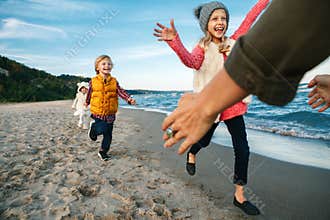 Three funny smiling laughing white Caucasian children kids friends playing running to mother parent adult on ocean sea beach